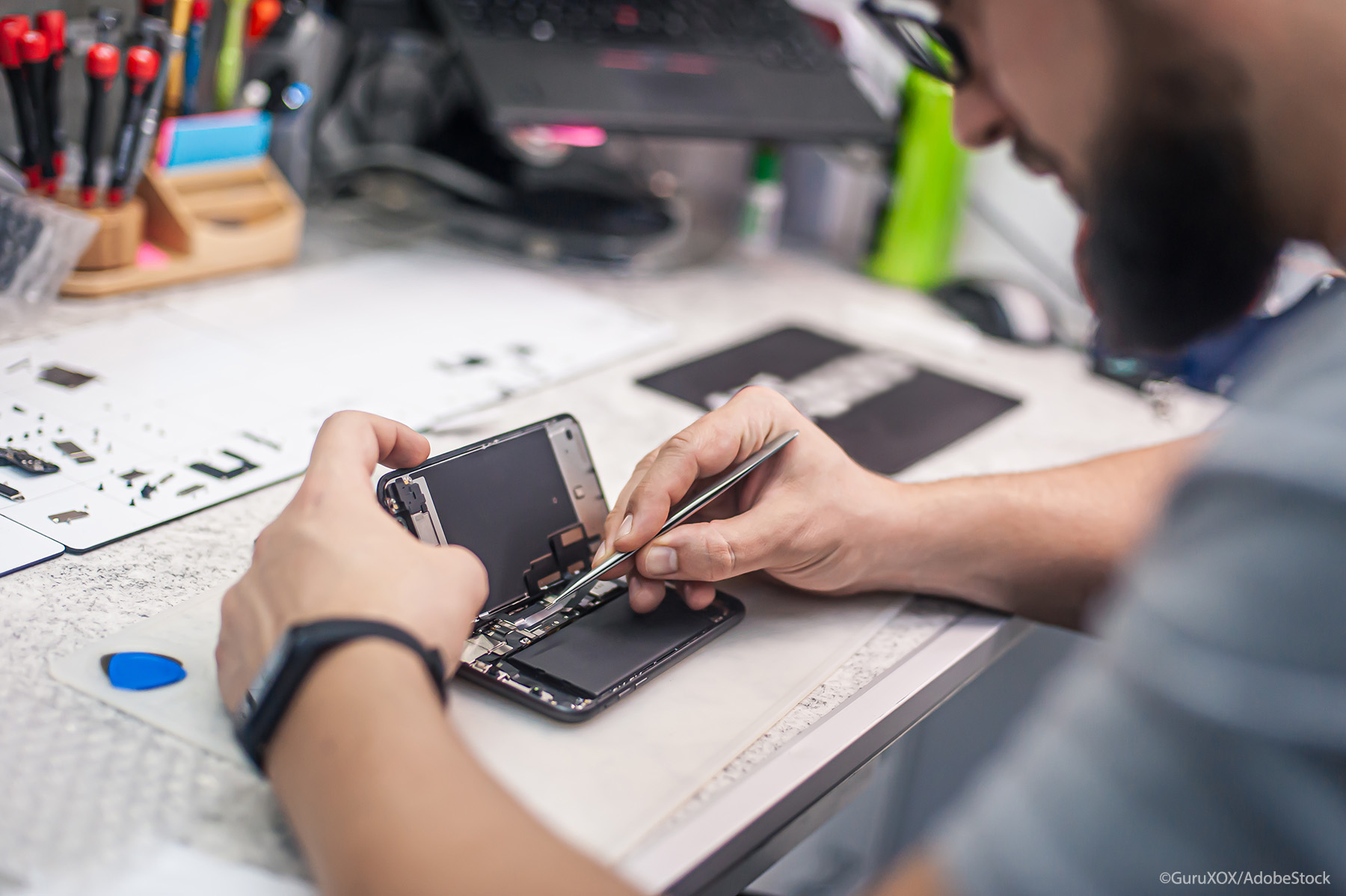 technician repairs smartphone, uses tweezers as tool in electronics workshop